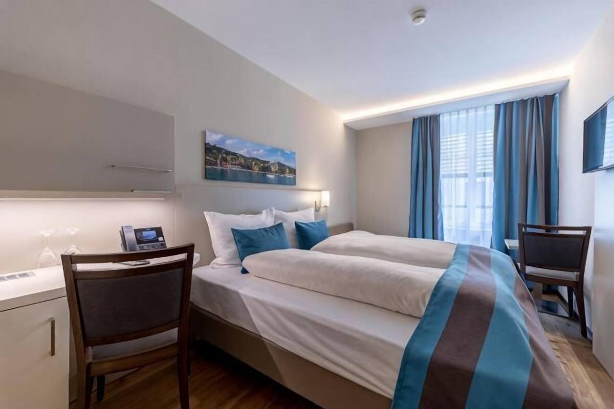 A hotel room with a bed, desk, chair, and a TV.