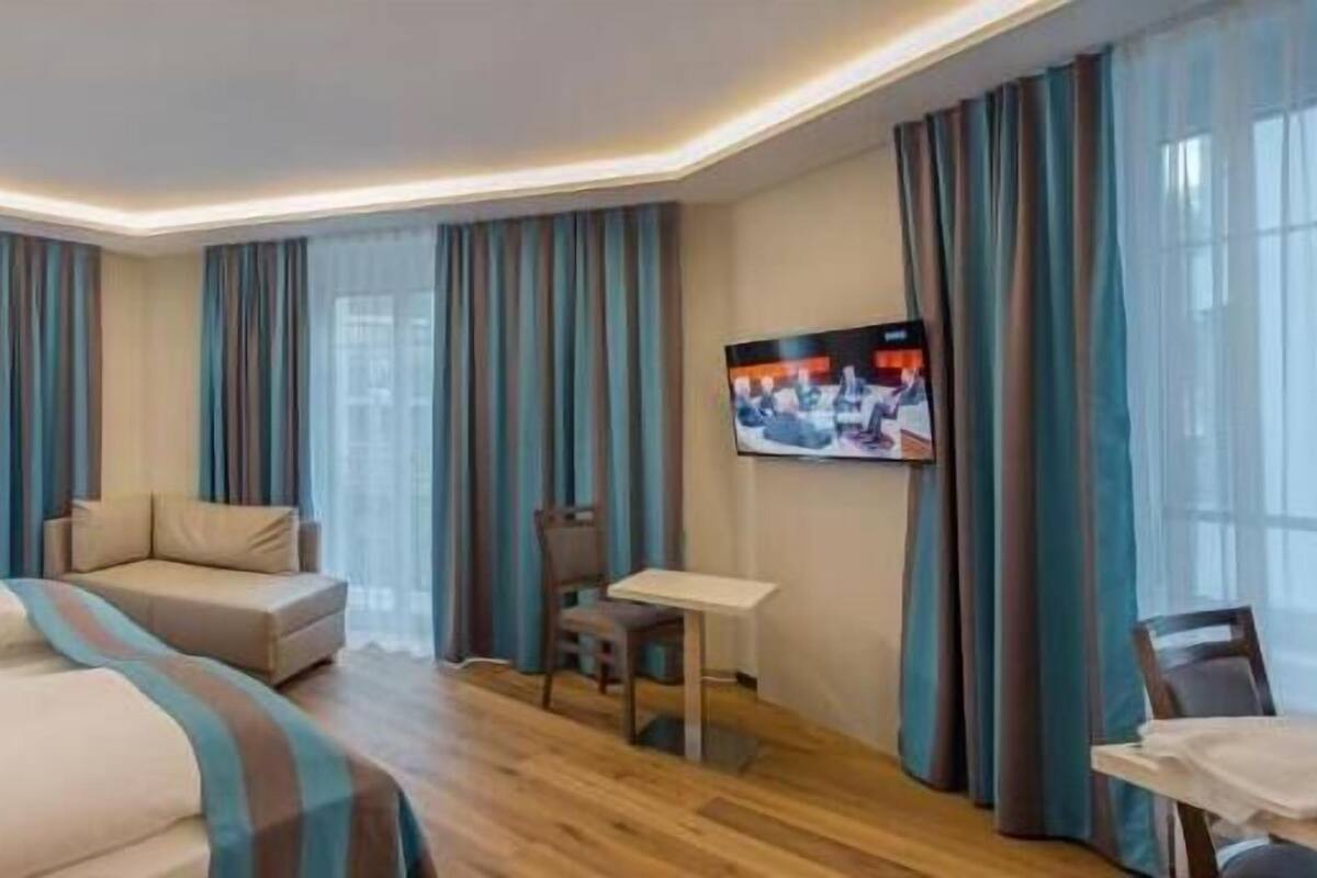 A hotel room with two beds, a sofa, a TV, and a small table.