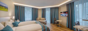 Quarto de hotel com duas camas, um sofá, uma televisão e uma mesinha.