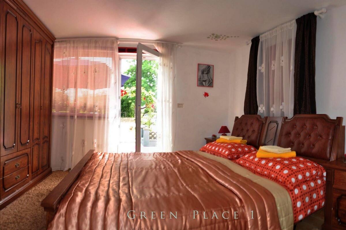 Un dormitorio con una cama grande, un armario, una mesita de noche con lámpara y una ventana con cortinas.