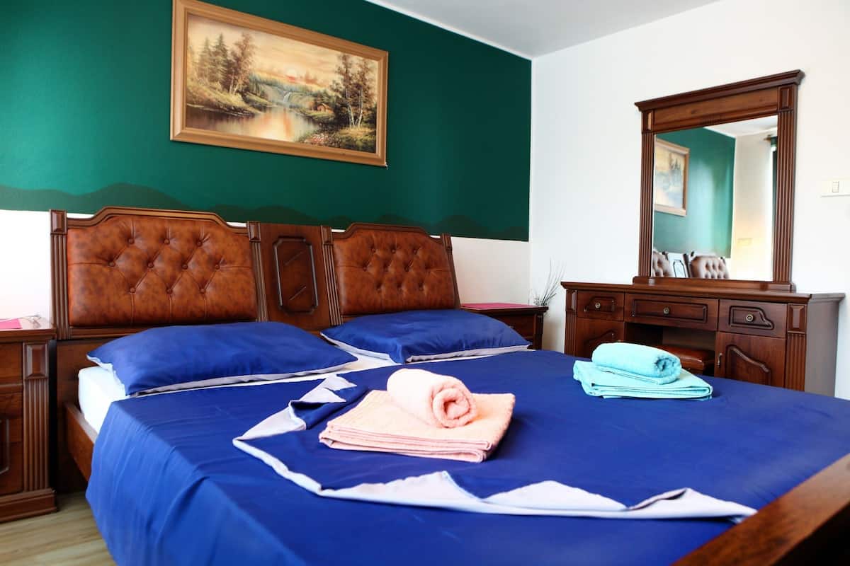Una cama bien hecha con ropa de cama azul y un cabecero de madera, un cuadro en la pared y un espejo sobre la cama.