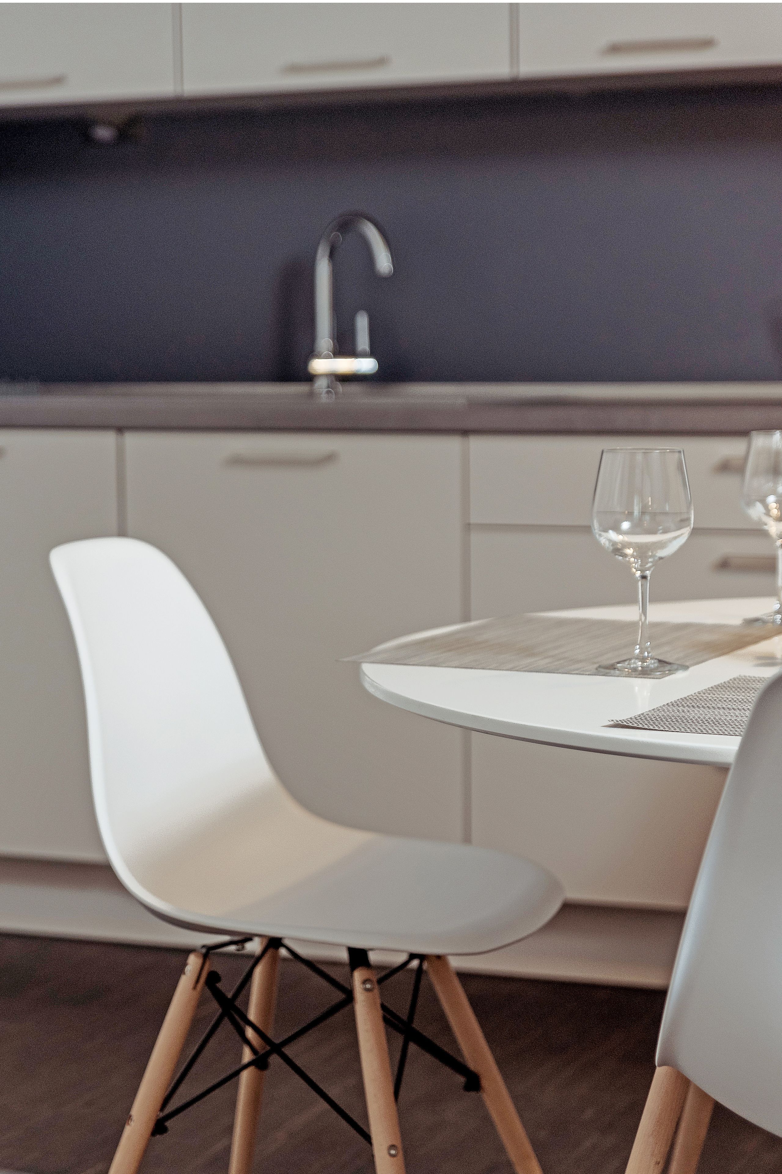 A modern kitchen with white cabinets, a dark backsplash, and a round dining table with a glass top.