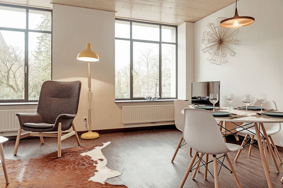 A modern living room with a large window, a cowhide rug, a dining table set for four, and a unique wall decoration.