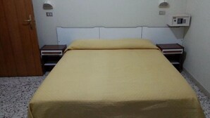 A single bed with a beige bedspread in a room with white walls, a wooden door, and two bedside tables with lamps. - Hotel Mutacita (Rimini)