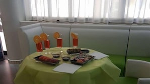 A dining area with a round table covered by a yellow tablecloth, surrounded by green cushioned seating. - Hotel Mutacita (Rimini)
