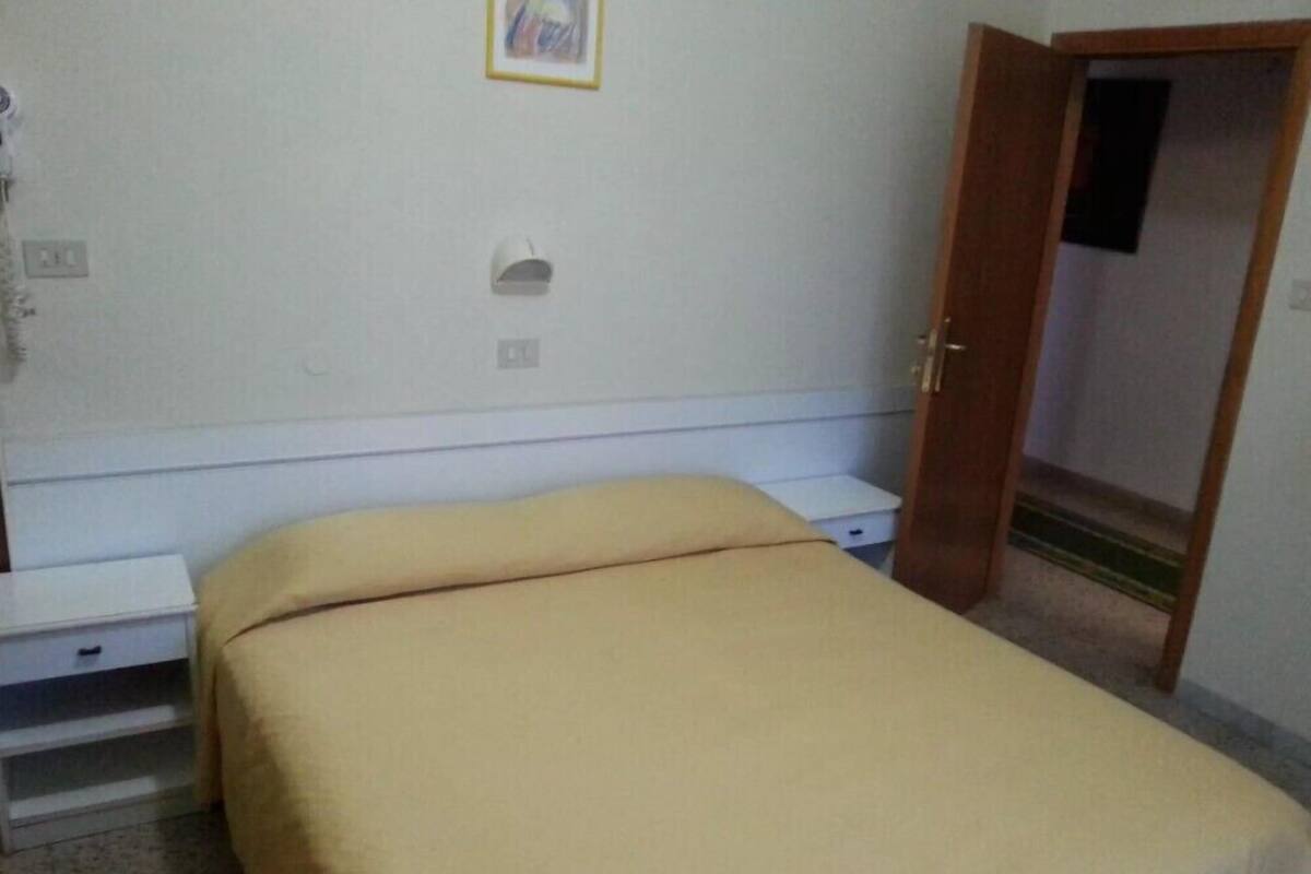 A bedroom with a bed, a nightstand, a wall-mounted light, and a door.
