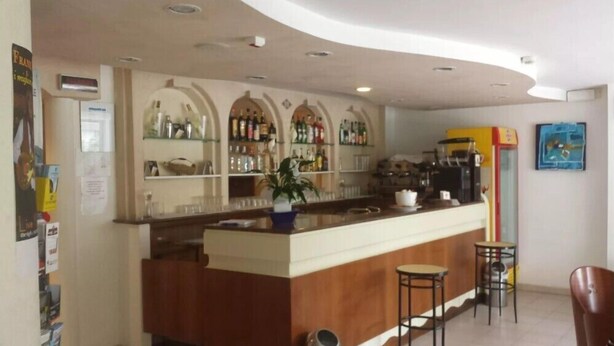 A bar area with a counter, stools, and shelves stocked with bottles. - Hotel Mutacita (Rimini)
