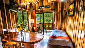 Un intérieur en bois comprenant un lit, un coin repas avec des tabourets, un téléviseur et une pancarte sur laquelle on peut lire : « Chez soi, on est bien ».