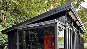 Une structure moderne et minimaliste, dotée d’un toit en pente, de grandes fenêtres en verre et d’une base en pierre.
