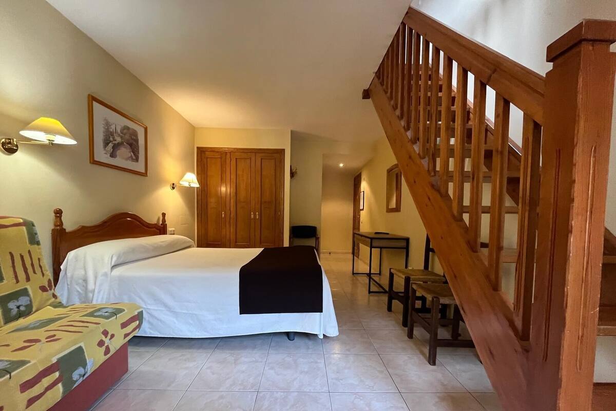 A bedroom with a bed, a wooden chair, a desk, and a staircase.