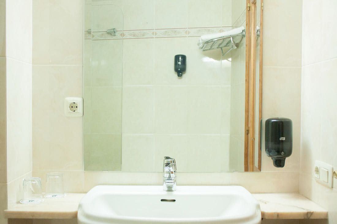 Een badkamer met een wastafel, spiegel en twee zeepdispensers.