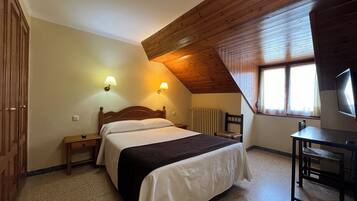 A bedroom with a bed, bedside tables, a chair, a desk, a television, and a window with blinds.