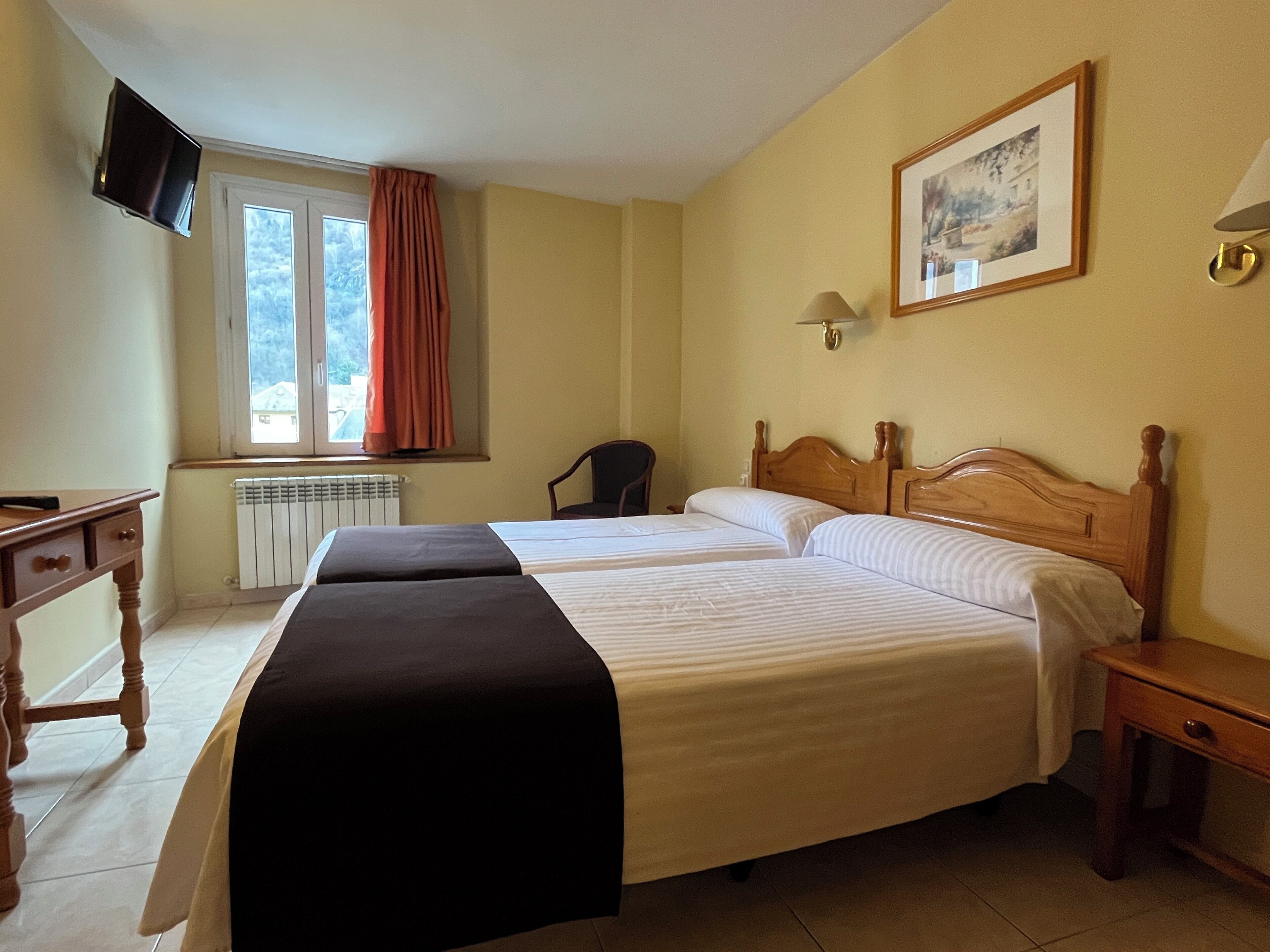 A hotel room with two beds, a desk, a chair, a television, and a window with curtains.