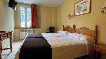 A hotel room with two beds, a desk, a chair, a television, and a window with curtains.