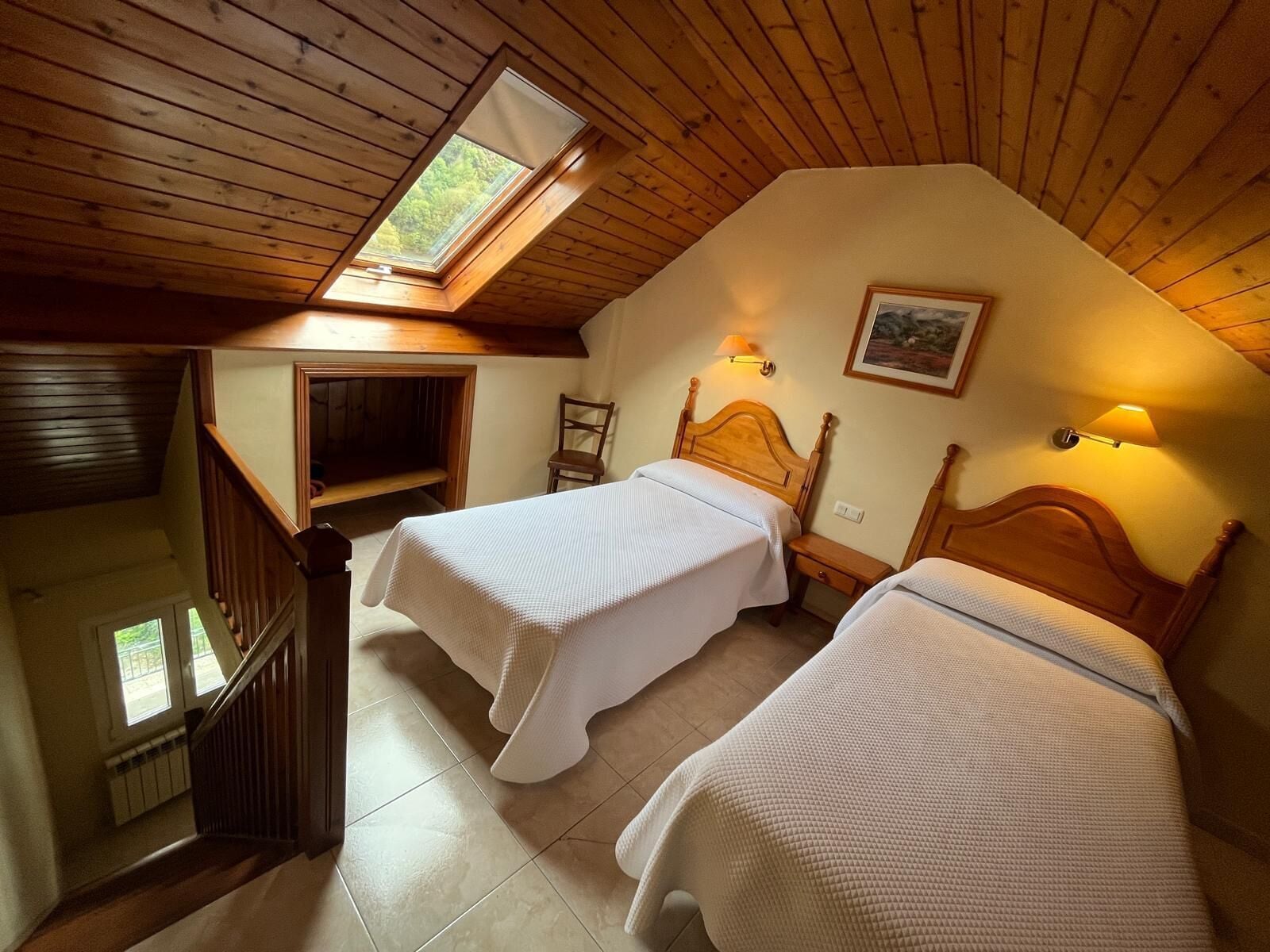 Um quarto de sótão acolhedor com duas camas, vigas de madeira, um claraboia e uma escada.