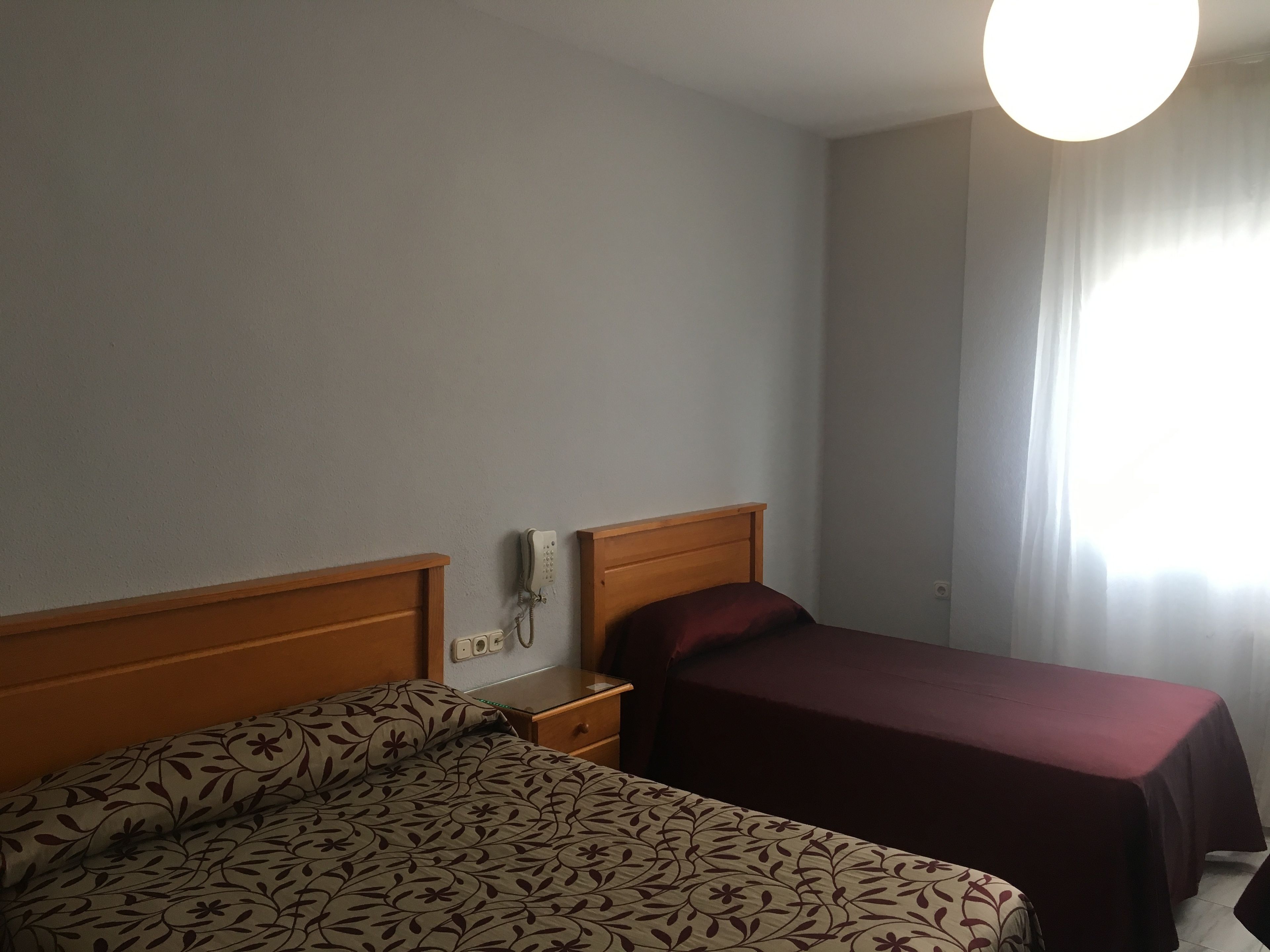 Habitació d'hotel amb dos llits, una taula de nit amb un telèfon i una finestra amb cortines.