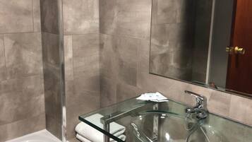 A modern bathroom with a glass-enclosed sink, a white bathtub, and a large mirror.