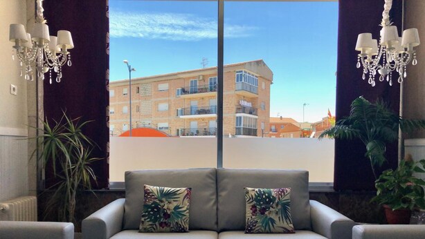 A modern living room with a grey sofa, two matching cushions, a glass coffee table, and a view of a building through large windows. - Hotel Santa Fe (Santa Fe)