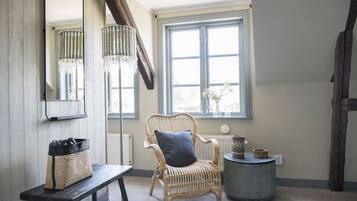 Une pièce comprenant un fauteuil en osier, un banc, une table ronde, un miroir et une fenêtre donnant sur des arbres.