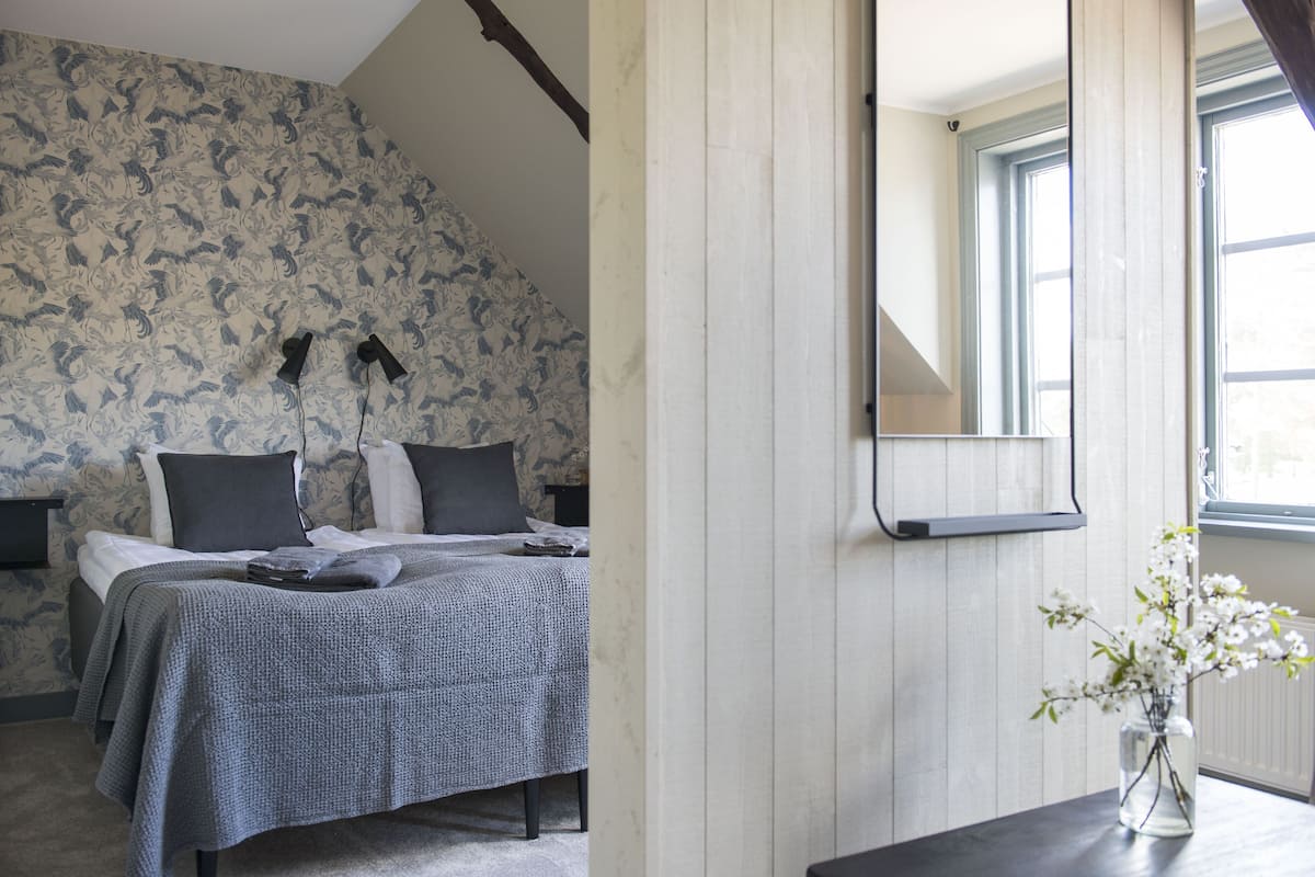 Quarto com cama, mesa de cabeceira, espelho e um vaso com flores.