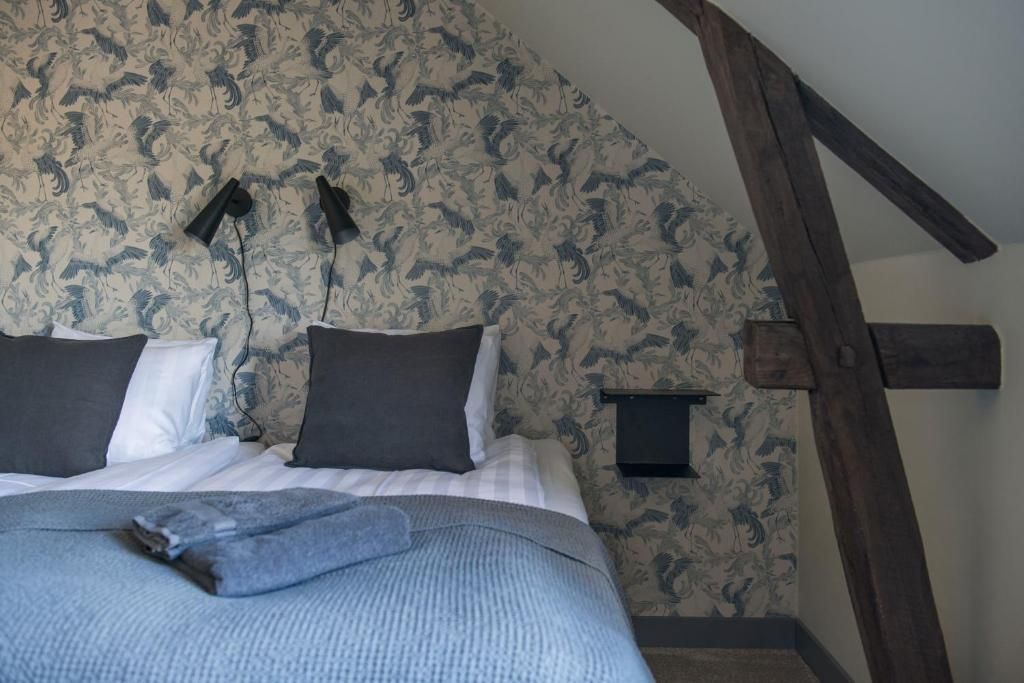 A bedroom with a sloped ceiling, a bed with a grey blanket, two black lamps, and a wall with a floral pattern.