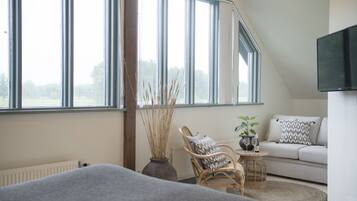 A cozy room with a large window, a sofa, a chair, a small table, and a vase with plants.