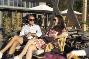 Two people sitting on wicker chairs outdoors, with a stone wall and umbrellas in the background. - Gumbalde Resort (Stånga)