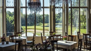Een eetgedeelte met tafels en stoelen, grote ramen met uitzicht op een golfbaan en hangende decoraties.