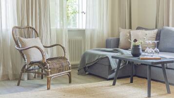 Una habitación con una silla de mimbre, un sofá gris y una mesa de centro con un florero y vasos.