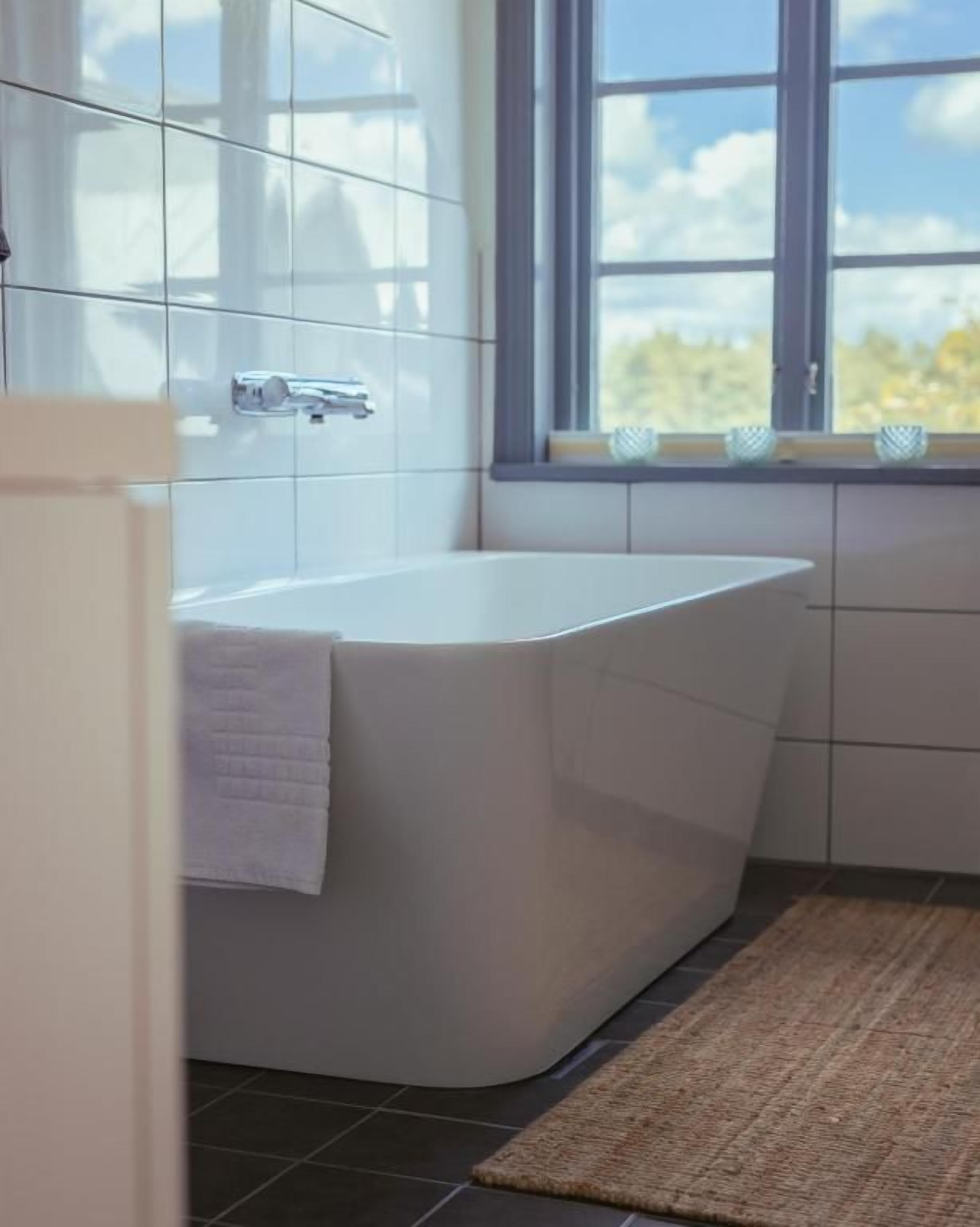 A modern bathroom with a freestanding bathtub, a window with a view, and a tiled floor.