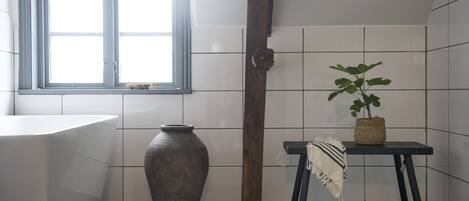 A bathroom with a bathtub, a large vase, a potted plant, and a window with a view.