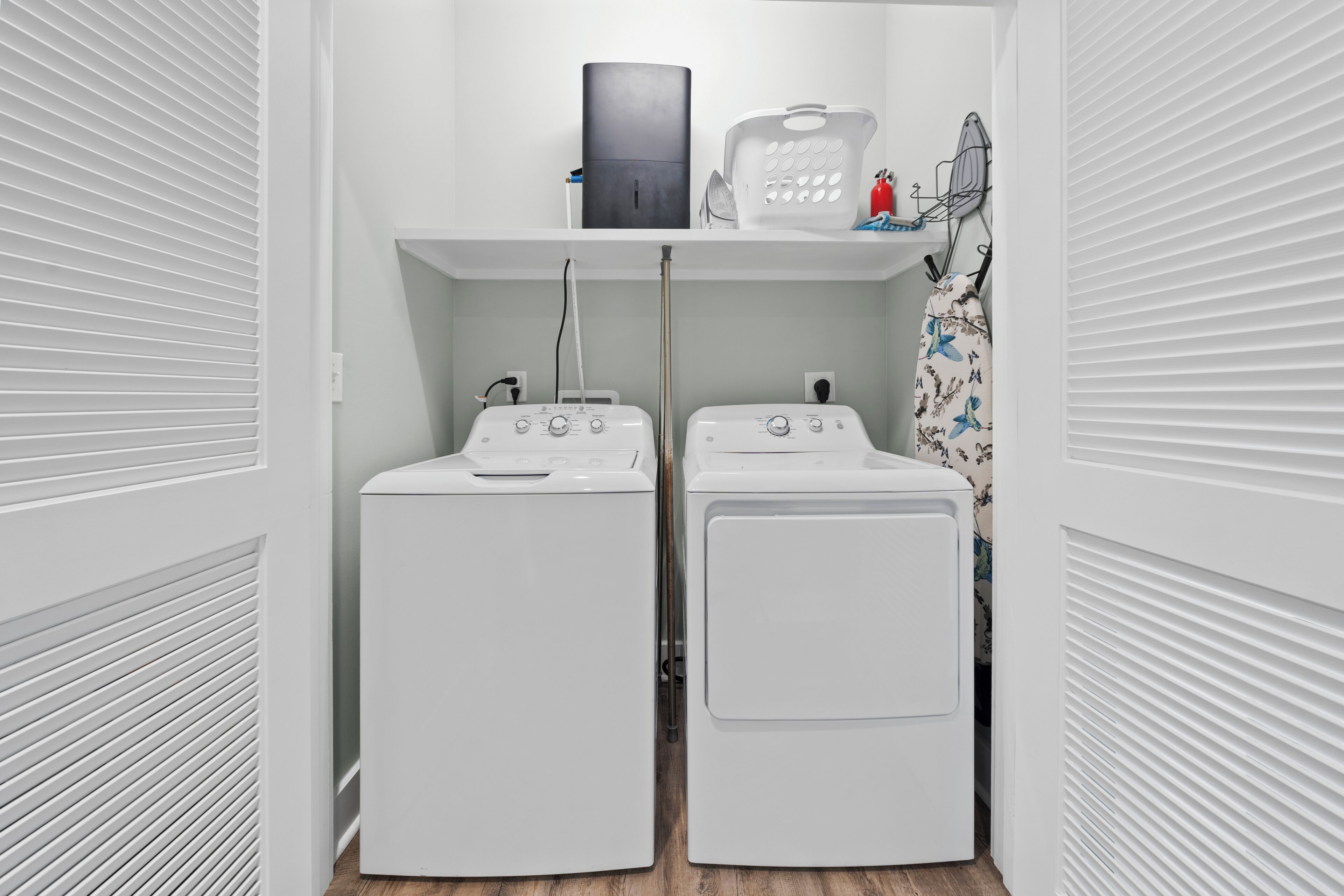 A laundry room with two white front-loading washing machines, a drying rack, and a fire extinguisher on the wall.