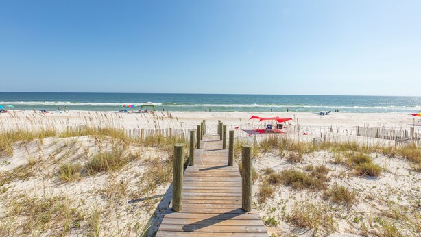A wooden boardwalk leading to a beach with sand dunes and a clear blue sky. - Little Lagoon Cottages (Gulf Shores)