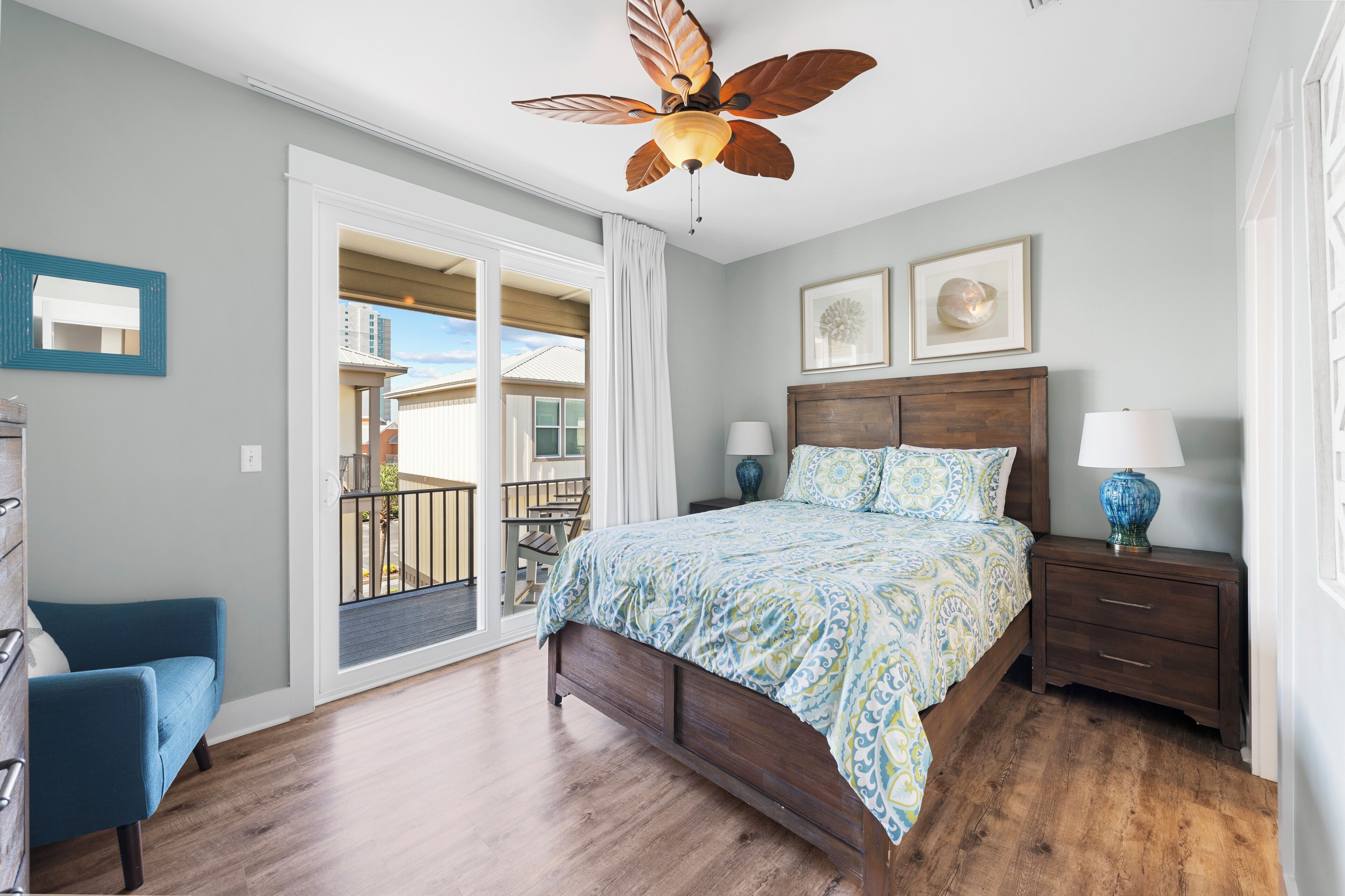 Une chambre à coucher comprenant un lit, des tables de chevet, un ventilateur de plafond, une fenêtre avec des rideaux et une vue sur l’extérieur.
