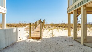 A wooden boardwalk leading to a building with a balcony, surrounded by sand and sparse vegetation. - Little Lagoon Cottages (Gulf Shores)