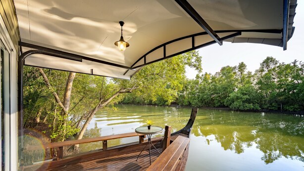 Una terraza de madera con una mesa y banco da a un río tranquilo, rodeada de exuberante vegetación.