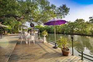 A wooden deck with outdoor seating and umbrellas overlooking a river.