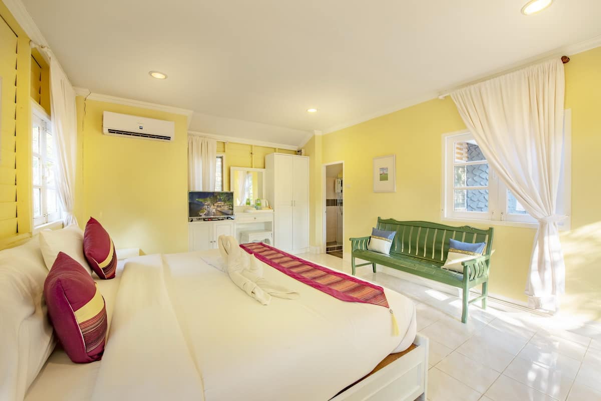 A hotel room with a bed, a green bench, a white wardrobe, and an air conditioning unit.