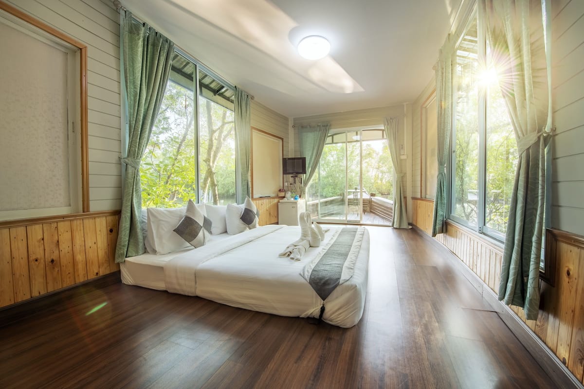 A spacious bedroom with a large bed, wooden floors, and large windows with curtains.