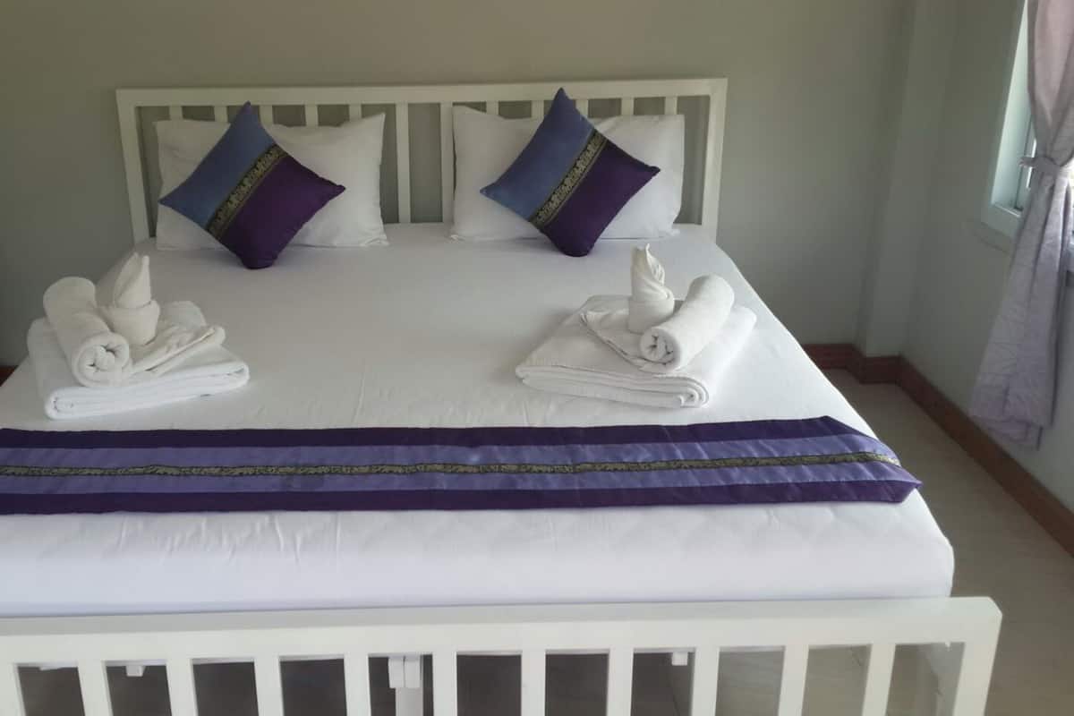 A neatly made bed with white linens, two pillows, and a folded towel on each side.