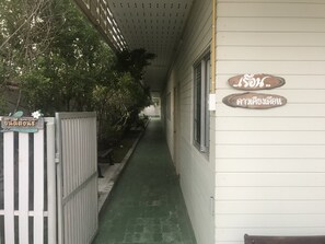 A narrow corridor with a green floor, a white fence, and a wooden sign with Thai text.