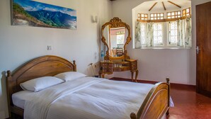 A bedroom with a wooden bed, a dresser, a mirror, and a window with curtains. - Mount Mary Inn (Nuwara Eliya)