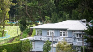 A two-story house with a grey roof, white window frames, and a stone wall in the foreground. - Mount Mary Inn (Nuwara Eliya)