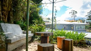 A garden area with a stone bench, wooden stools, and a concrete planter. - Mount Mary Inn (Nuwara Eliya)