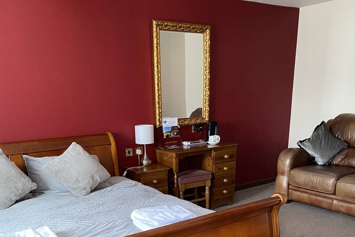 Une chambre à coucher avec un lit en bois, un bureau avec une chaise, un canapé en cuir et un grand miroir.