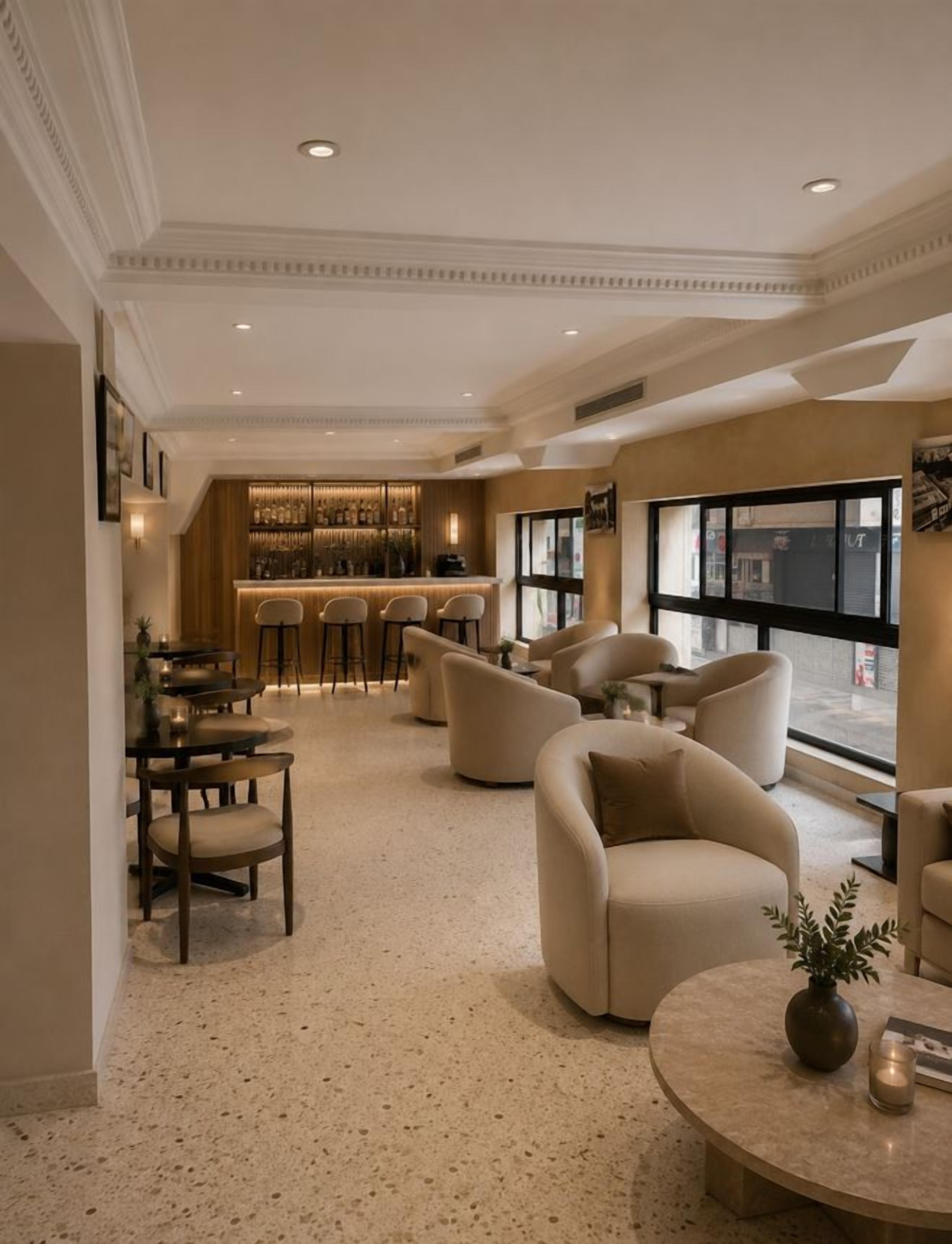 Un hall d’hôtel comprenant un bar, des espaces aménagés avec des sièges et offrant une vue sur l’extérieur grâce à de grandes fenêtres.