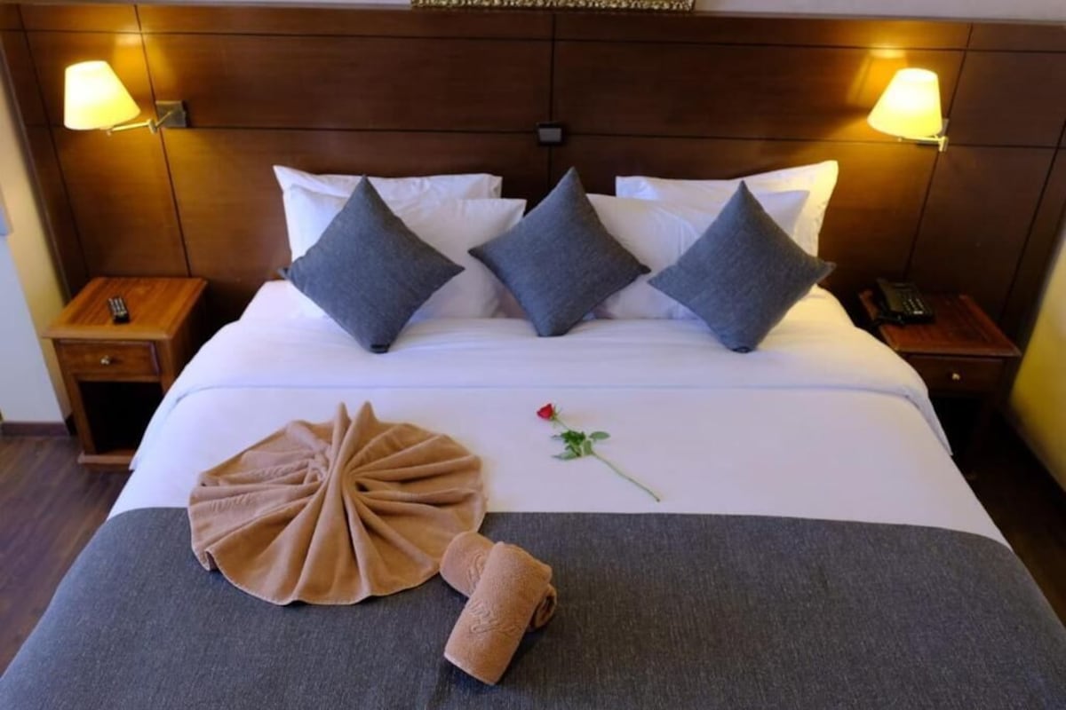 Una cama bien tendida con una toalla marrón y una rosa sobre el edredón.