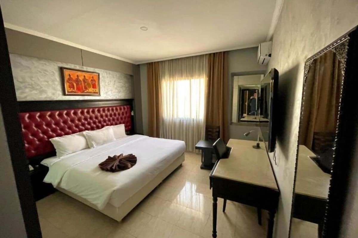 Una habitación de hotel con una cama grande, un escritorio, un espejo y un cuadro en la pared.