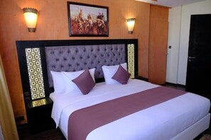 Una cama grande con cabecera capitonada, dos mesitas de noche y un cuadro sobre la cama.