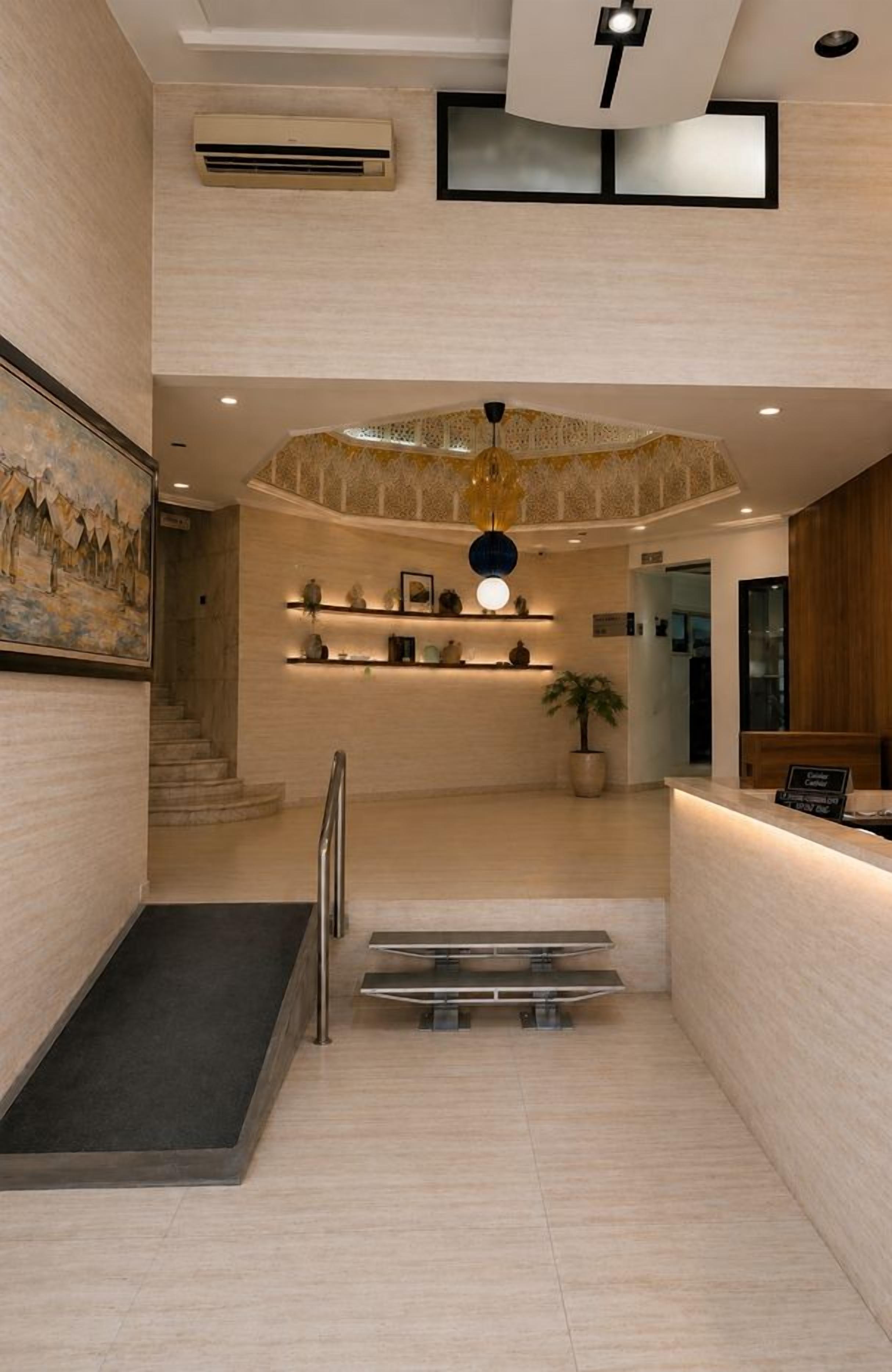 Un hall d’hôtel avec un escalier, un comptoir d’accueil et un lustre décoratif au plafond.